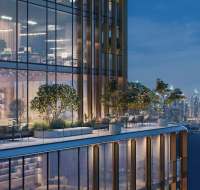 Glass-fronted building with a shared outdoor patio, captured during the evening with lights visible inside and across the water.