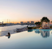 Infinity pool overlooking a marina with yachts and a panoramic city skyline view at sunset.