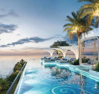 A luxurious infinity pool overlooking the ocean at sunset, surrounded by sun loungers and palm trees.
