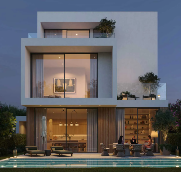 Rear view of a modern villa at Chevalia Estate 2, showing the backyard with a swimming pool and illuminated patio area at dusk.