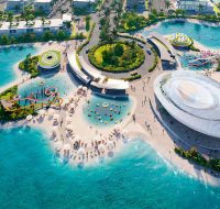 An outdoor leisure hub with water slides, a sandy beach, and various recreational facilities surrounded by clear blue water.