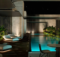 A serene rooftop pool with glowing blue water, surrounded by tropical plants and modern lounge chairs.