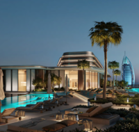 Rooftop infinity pool and lounge deck at twilight with a view of the ocean and the Burj Al Arab hotel.