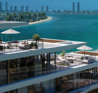 Residential buildings with tiered balconies viewed from a serene, crescent-shaped beach and clear blue water.