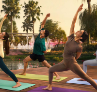 A group of people practicing yoga on a wooden deck near a fountain at sunrise or sunset .