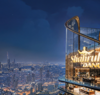 A tall, distinctive commercial skyscraper in Dubai with a curved facade, overlooking a busy highway and the city skyline at night.