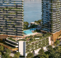 Two modern waterfront residential towers with lush green terraces and a large swimming pool deck overlooking the sea, surrounded by dense greenery.