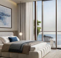 Modern bedroom with floor-to-ceiling windows, a plush bed with neutral bedding, contemporary artwork, and a balcony overlooking the sea.