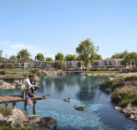 Residential park area featuring a clear water pond surrounded by flowering plants and townhouses in the background.